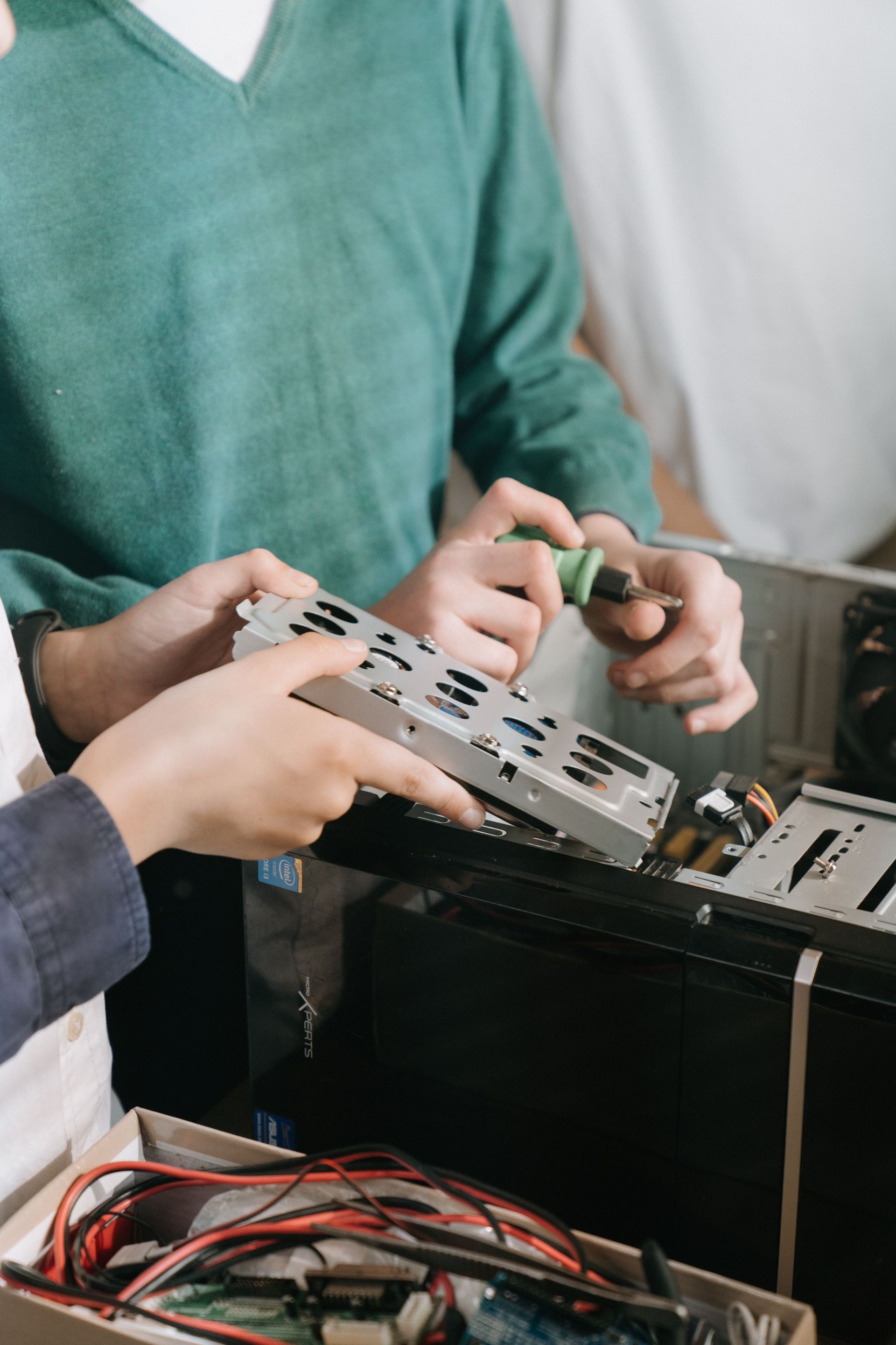 Close-up of technicians repairing computer hardware with tools, focusing on hands and equipment.